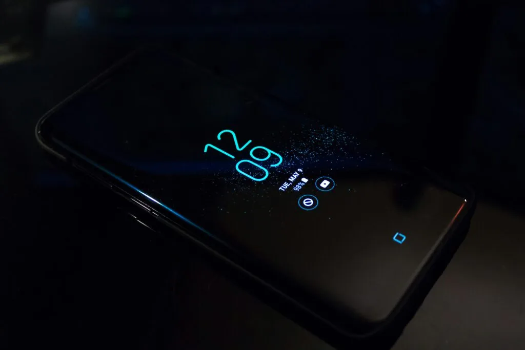Close-up of a smartphone in the dark displaying digital clock and notifications.